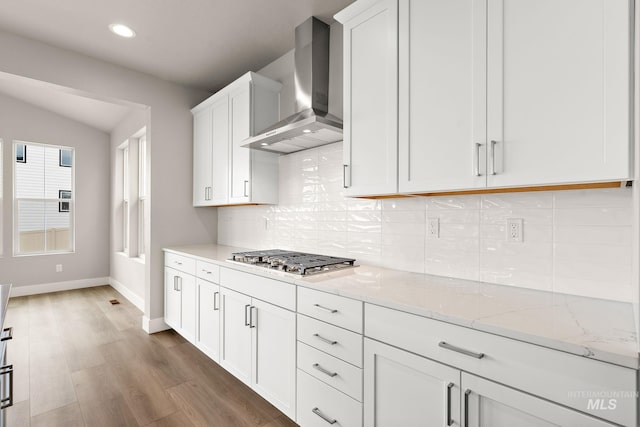 kitchen featuring light stone countertops, stainless steel gas cooktop, dark wood-type flooring, white cabinets, and wall chimney range hood