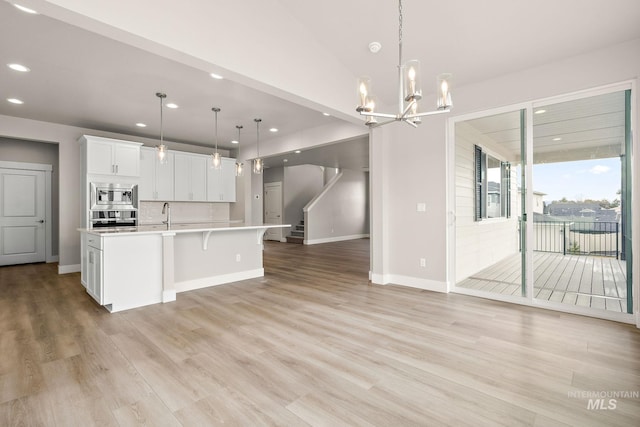 kitchen featuring light wood-style flooring, stainless steel appliances, light countertops, white cabinetry, and open floor plan