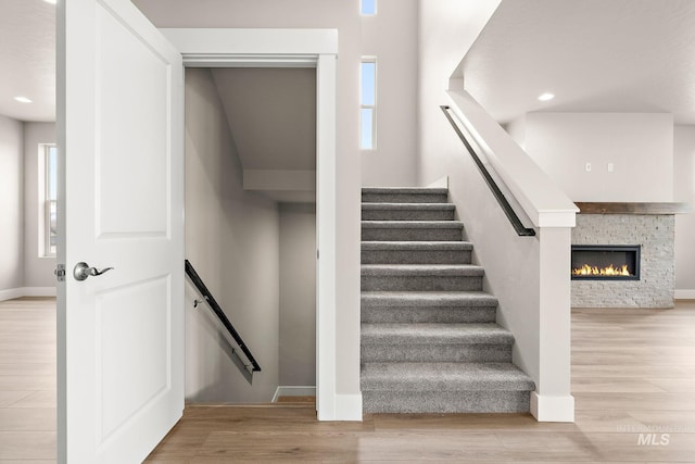 staircase featuring plenty of natural light, a stone fireplace, baseboards, and wood finished floors