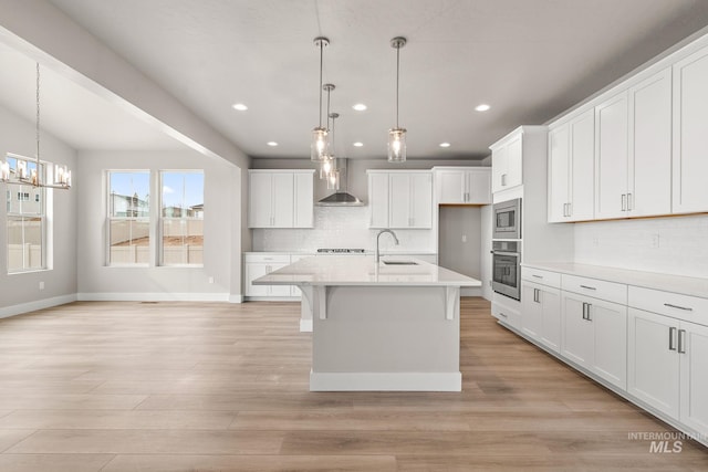 kitchen with wall chimney range hood, light wood-style floors, appliances with stainless steel finishes, and a sink