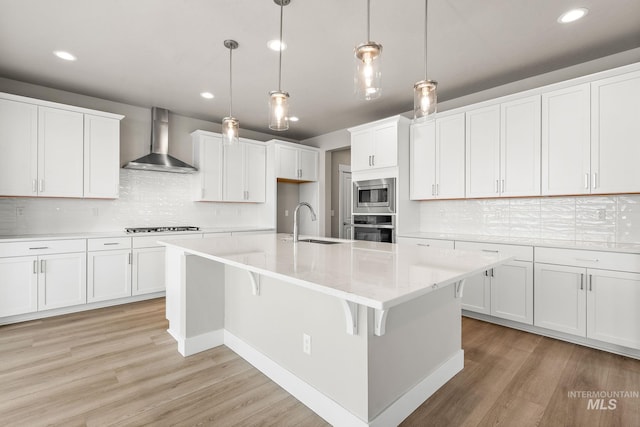 kitchen with a sink, light wood-style flooring, wall chimney exhaust hood, and stainless steel appliances