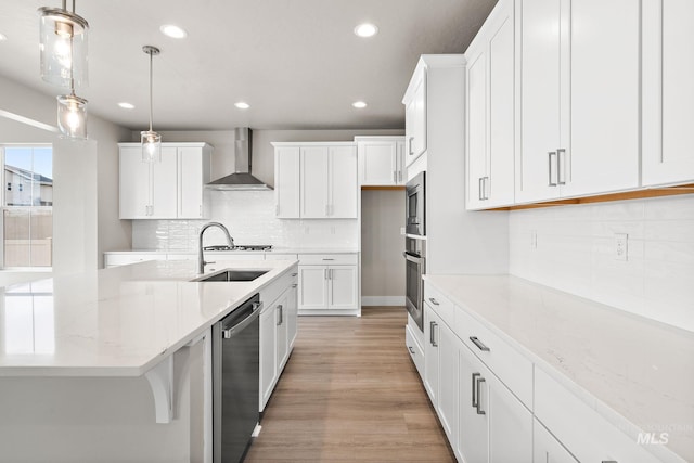 kitchen featuring light wood-type flooring, a sink, white cabinetry, appliances with stainless steel finishes, and wall chimney range hood