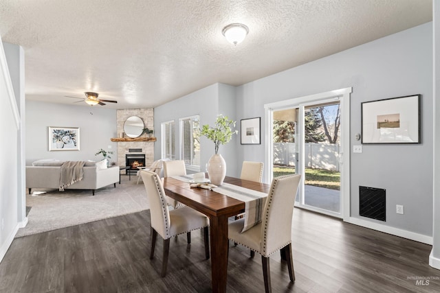 dining area with a textured ceiling, a fireplace, dark wood finished floors, and baseboards