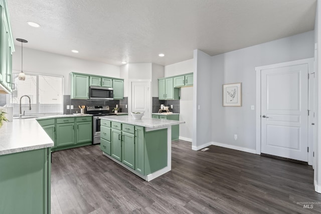 kitchen with dark wood-style floors, a sink, stainless steel appliances, green cabinets, and backsplash