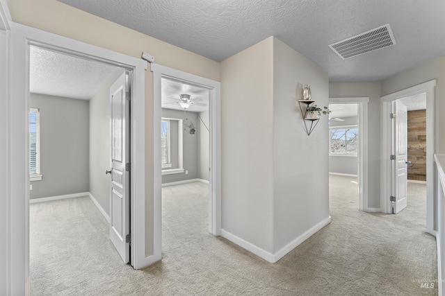 hall with a textured ceiling, carpet flooring, visible vents, and baseboards