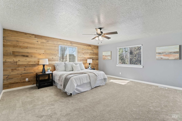 carpeted bedroom with a textured ceiling, wooden walls, baseboards, and a ceiling fan