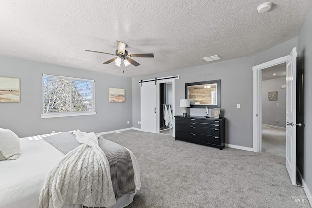 carpeted bedroom featuring a barn door, visible vents, baseboards, ceiling fan, and a textured ceiling