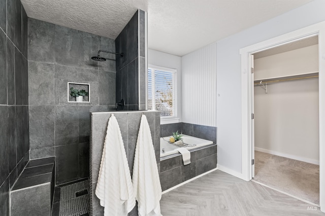 full bathroom with a textured ceiling, a garden tub, baseboards, a walk in closet, and walk in shower