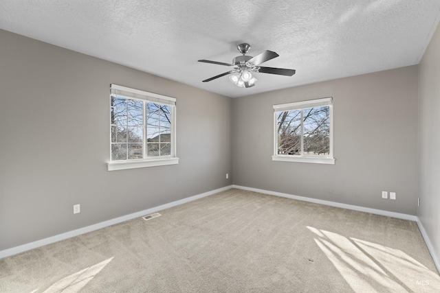 carpeted spare room featuring visible vents, a textured ceiling, baseboards, and a ceiling fan