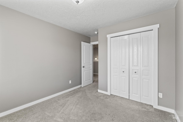 unfurnished bedroom with a textured ceiling, carpet floors, a closet, and baseboards