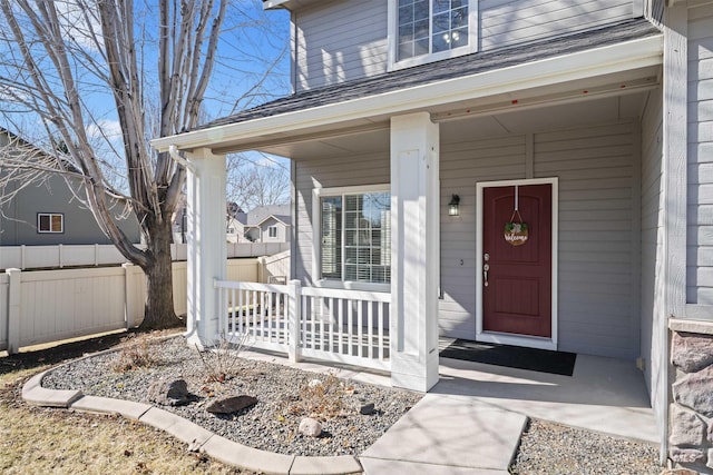 view of exterior entry featuring a porch and fence