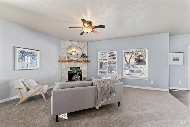 carpeted living area featuring ceiling fan, baseboards, a textured ceiling, and a stone fireplace