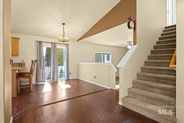 foyer entrance with ceiling fan with notable chandelier, dark wood-type flooring, plenty of natural light, and lofted ceiling