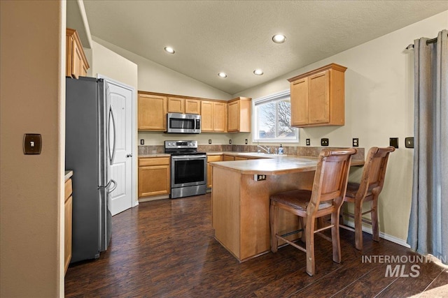 kitchen with kitchen peninsula, a breakfast bar, stainless steel appliances, dark wood-type flooring, and lofted ceiling