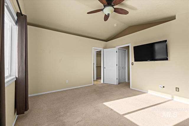 unfurnished bedroom with ceiling fan, light colored carpet, a walk in closet, and vaulted ceiling