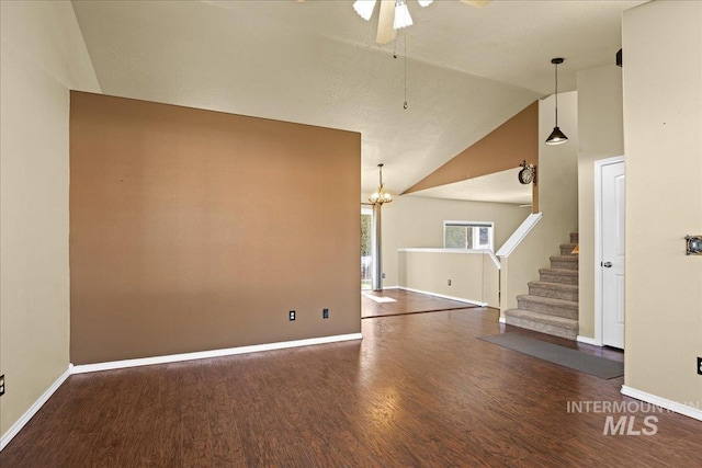 unfurnished living room featuring dark hardwood / wood-style floors, lofted ceiling, and ceiling fan with notable chandelier