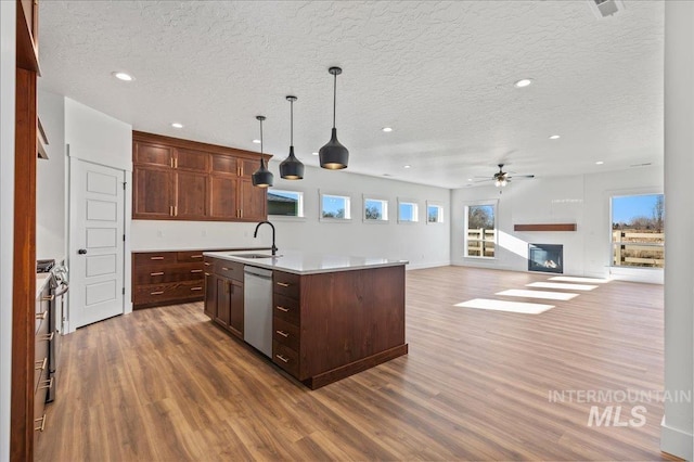 kitchen featuring a kitchen island with sink, stainless steel appliances, open floor plan, light countertops, and hanging light fixtures