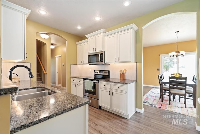 27482 Warren Ln, Wilder, ID 83676 - kitchen with stainless steel appliances, arched walkways, white cabinetry, dark stone countertops, and light wood finished floors
