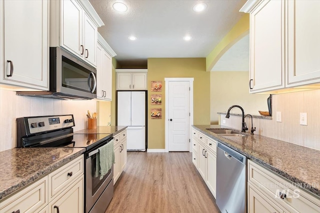 27482 Warren Ln, Wilder, ID 83676 - kitchen featuring stainless steel appliances, light wood-style flooring, arched walkways, white cabinets, and dark stone countertops