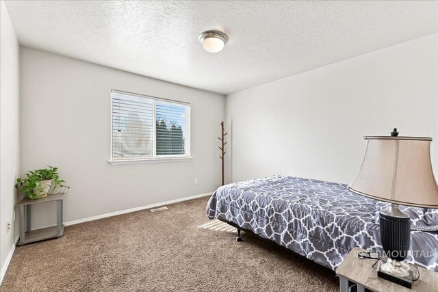 bedroom featuring visible vents, baseboards, carpet floors, and a textured ceiling