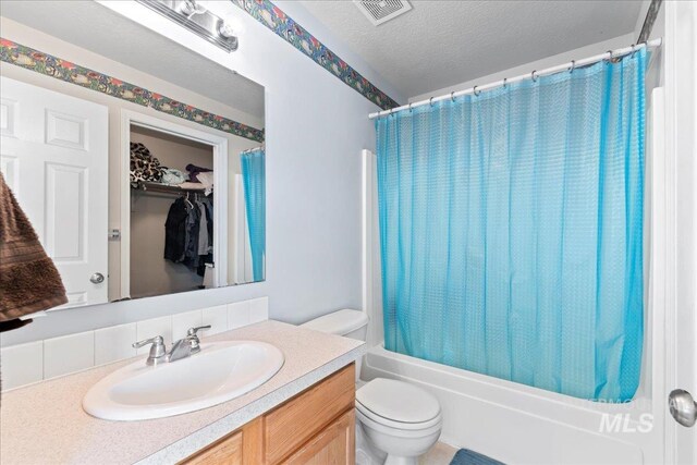 full bathroom with visible vents, shower / bath combo with shower curtain, toilet, vanity, and a textured ceiling