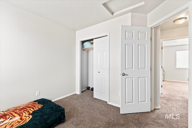 bedroom featuring baseboards, attic access, carpet floors, a closet, and a textured ceiling