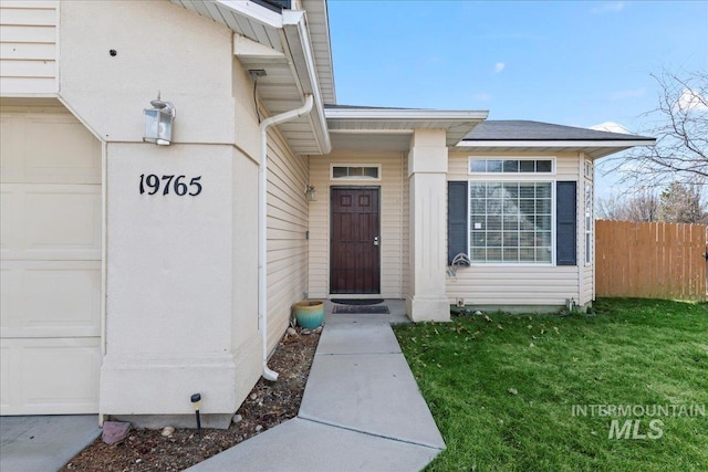 view of exterior entry with a lawn, an attached garage, and fence