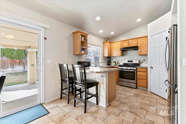 kitchen featuring under cabinet range hood, open shelves, a sink, appliances with stainless steel finishes, and a peninsula