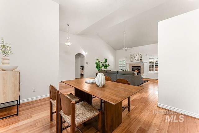 1730 W Glade Creek St, Meridian, ID 83646 - dining room featuring arched walkways, light wood finished floors, a warm lit fireplace, a ceiling fan, and high vaulted ceiling