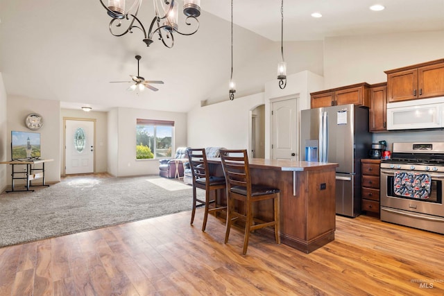 kitchen with stainless steel appliances, arched walkways, brown cabinetry, open floor plan, and a kitchen bar