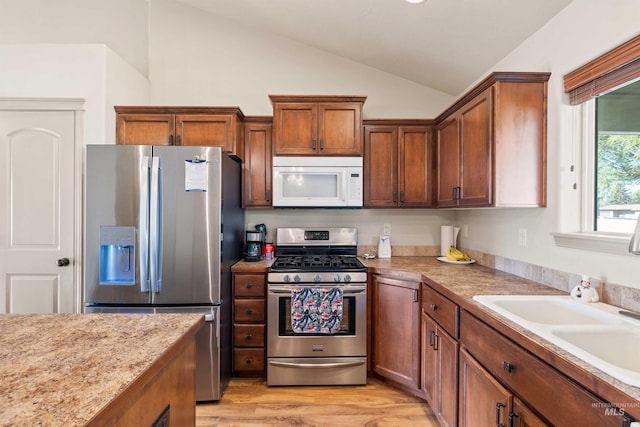kitchen featuring stainless steel appliances, vaulted ceiling, light countertops, brown cabinetry, and light wood-style floors