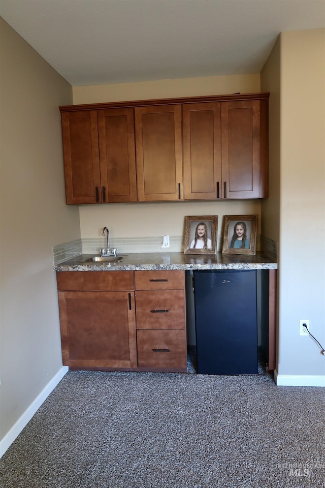 kitchen featuring dark colored carpet, light stone counters, and sink