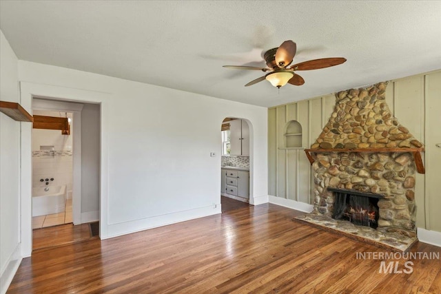 519 S 5th Ave, Nampa, ID 83651 - unfurnished living room with a ceiling fan, wood finished floors, a fireplace, arched walkways, and a textured ceiling
