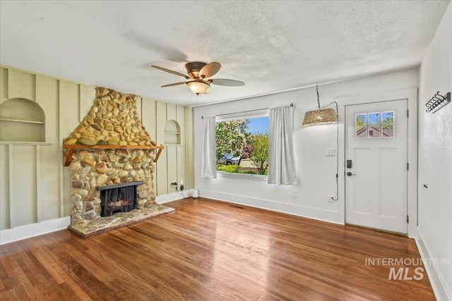 519 S 5th Ave, Nampa, ID 83651 - unfurnished living room featuring ceiling fan, wood finished floors, built in shelves, a stone fireplace, and a textured ceiling