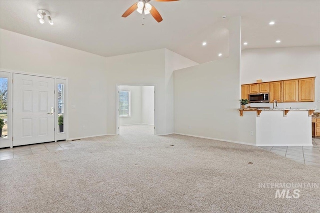 unfurnished living room featuring light carpet, light tile patterned floors, baseboards, and high vaulted ceiling