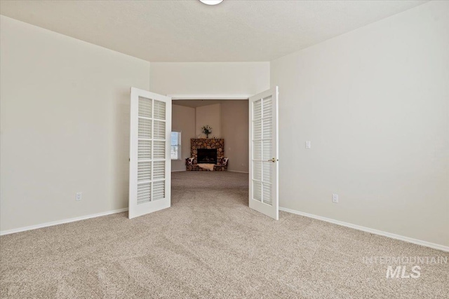 unfurnished room featuring french doors, light carpet, a fireplace, and baseboards