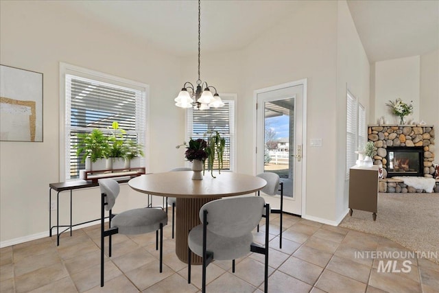 dining area featuring light tile patterned floors, a chandelier, a stone fireplace, light carpet, and baseboards