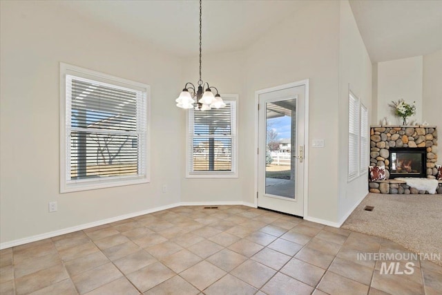 unfurnished dining area featuring light tile patterned floors, visible vents, baseboards, a stone fireplace, and a chandelier