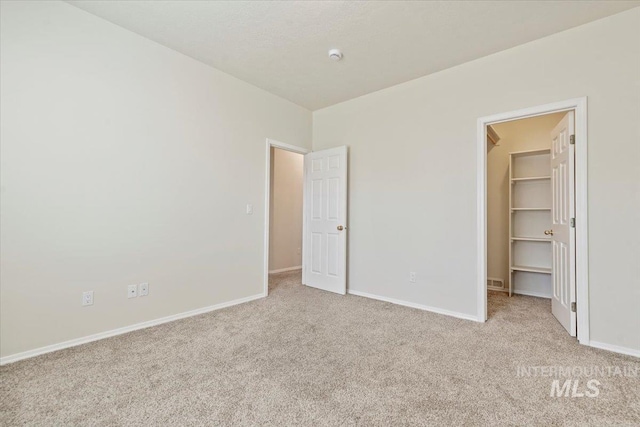 unfurnished bedroom with a walk in closet, a closet, light carpet, and baseboards