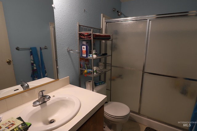 full bath featuring toilet, a textured wall, vanity, and a stall shower