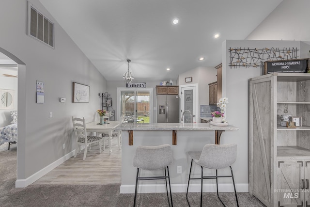 kitchen featuring a peninsula, arched walkways, baseboards, visible vents, and stainless steel fridge with ice dispenser