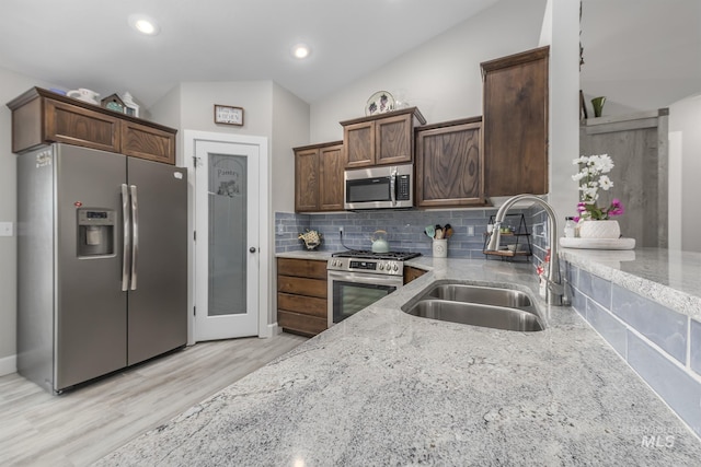 kitchen featuring vaulted ceiling, a sink, light wood-style flooring, appliances with stainless steel finishes, and light stone countertops