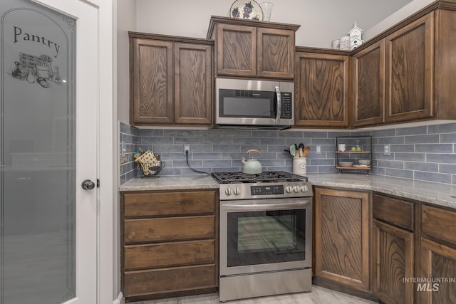 kitchen featuring light stone counters, dark brown cabinetry, appliances with stainless steel finishes, and tasteful backsplash