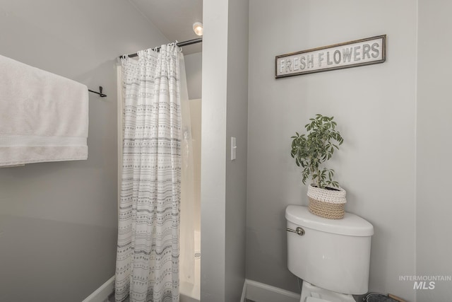 bathroom featuring shower / bath combination with curtain, toilet, and baseboards