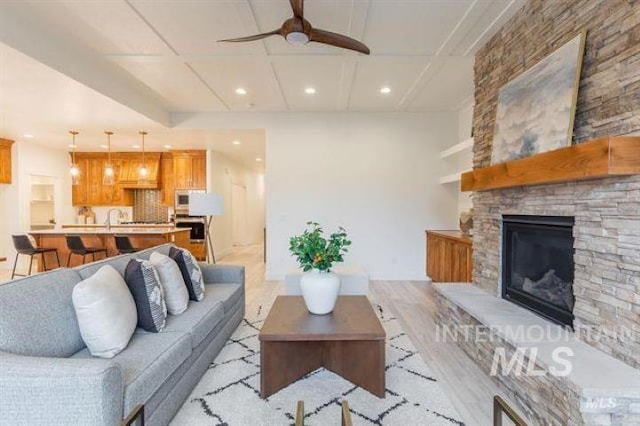 living room with a fireplace, light hardwood / wood-style floors, ceiling fan, and sink