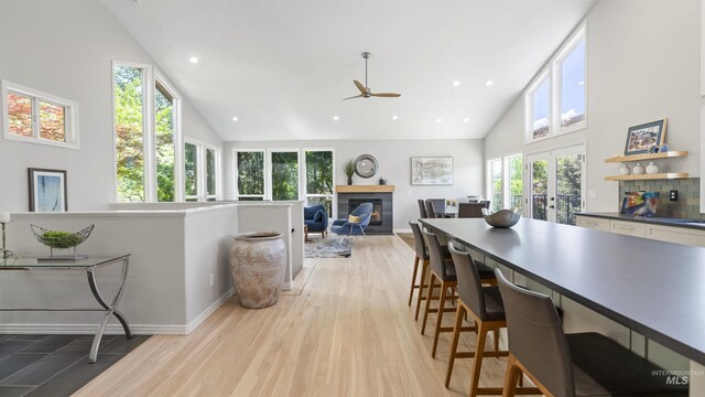 dining area with high vaulted ceiling, light wood-style flooring, ceiling fan, french doors, and a glass covered fireplace