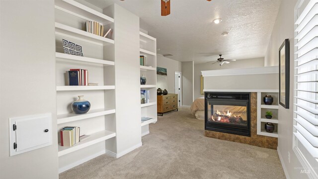 carpeted living room featuring ceiling fan, a multi sided fireplace, a textured ceiling, and built in shelves