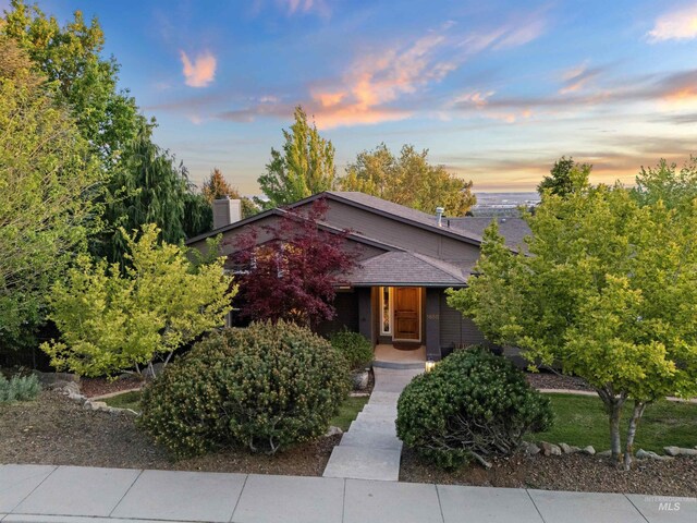 view of property hidden behind natural elements featuring roof with shingles and a chimney