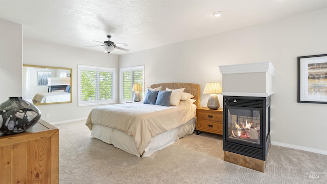 bedroom featuring a multi sided fireplace, carpet, baseboards, and a ceiling fan