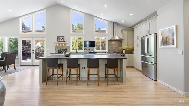 kitchen featuring high quality fridge, wall chimney range hood, dark countertops, a center island, and light wood finished floors